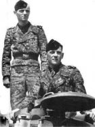 Bobby Woll en la cúpula de comandante junto a su conductor en pie sobre el carro de combate.