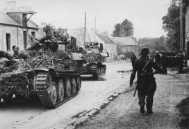 Varios Flakpanzer 38(t) cubiertos de ramas en marcha por un pueblo de Normandía. Los soldados alemanes estaban instruidos en camuflar sus vehículos con ramas.